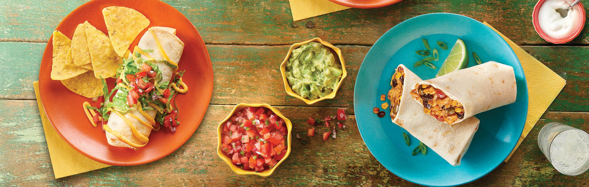 burritos serviti su piatti arancioni e blu con salsa di pomodoro e guacamole su un tavolo di legno rustico